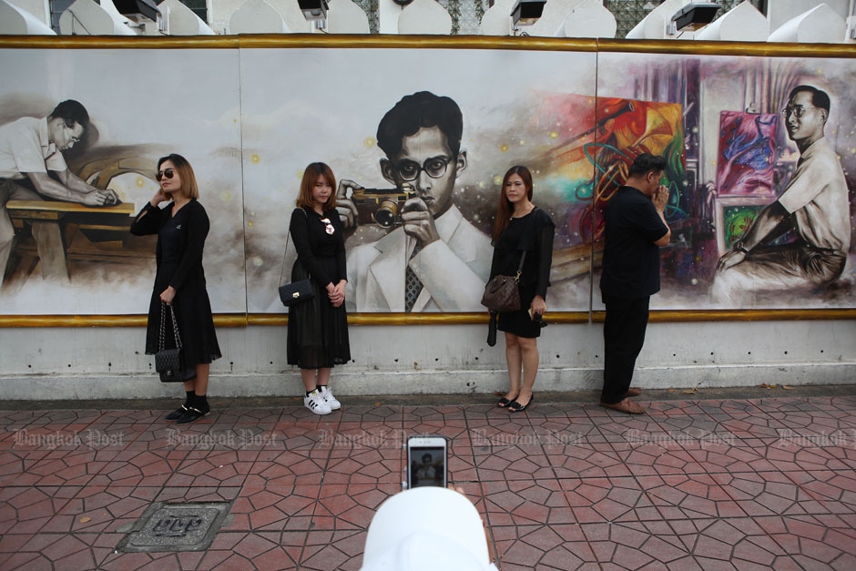 Mourners pay respect and pose for photos with the paintings of King Bhumibol on the wall of Silpakorn University near the Grand Palace.