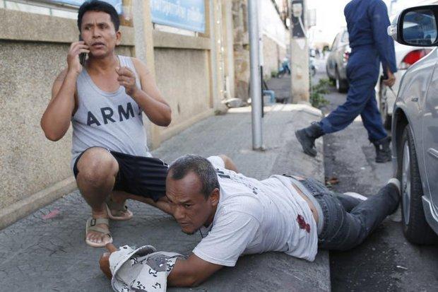 A wounded man lies on the ground grasping his injured arm as a friend phones for help after two more bombs went off near the Hua Hin clock tower Friday morning. Two people were killed in the resort town on Thursday night and Friday morning. (EPA photo)